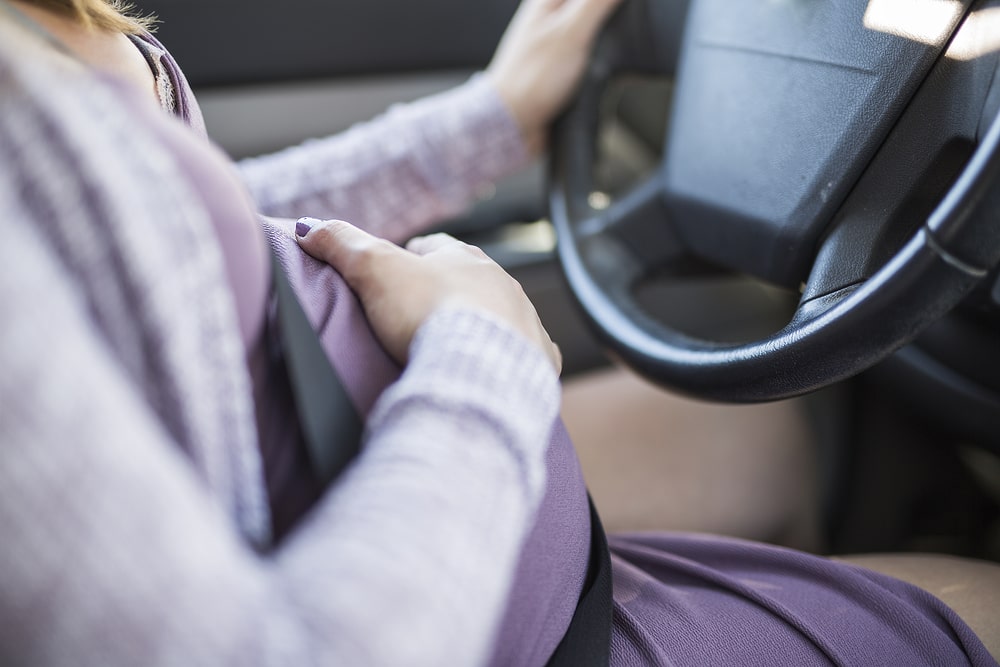 Pregnant Woman Sitting By The Wheel Of A Car