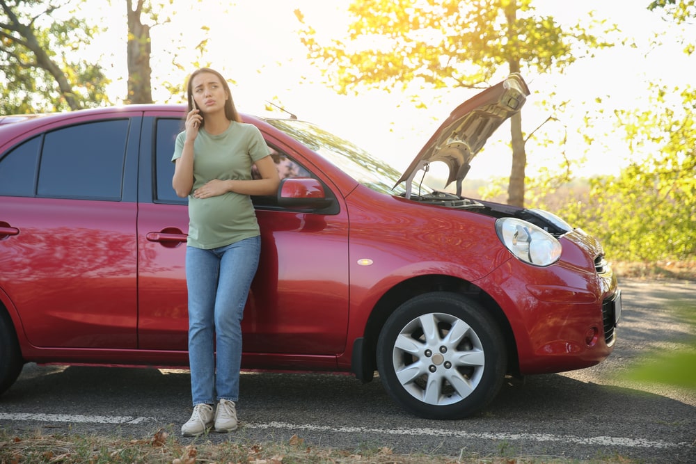 A Pregnant Woman Talking On The Phone Next To A Broken Down Car