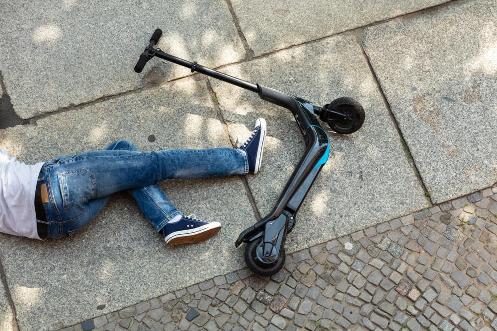 A Person Laying On The Ground Next To His Scooter